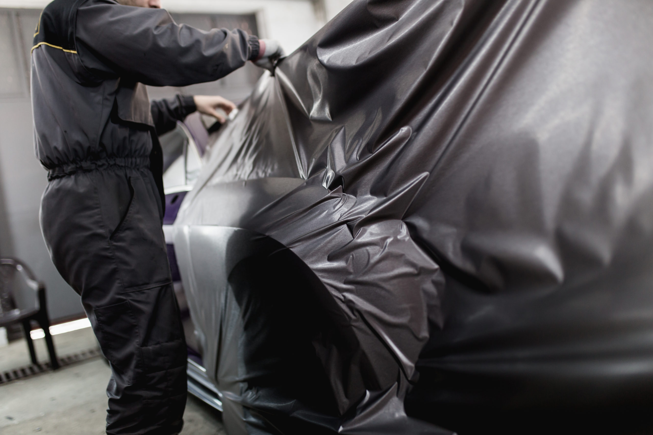 Car wrapping specialist putting vinyl foil or film on car. Selective focus.